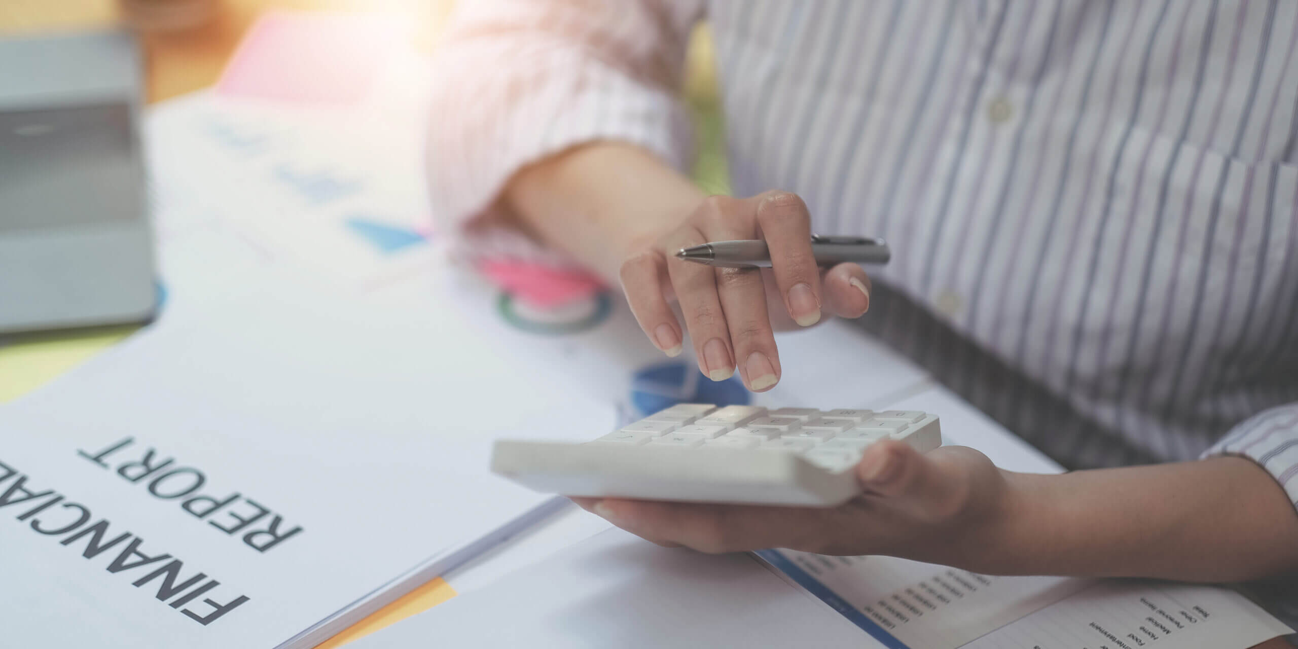 Person calculating numbers on a calculator beside financial reports, representing payroll management and accounting tasks.