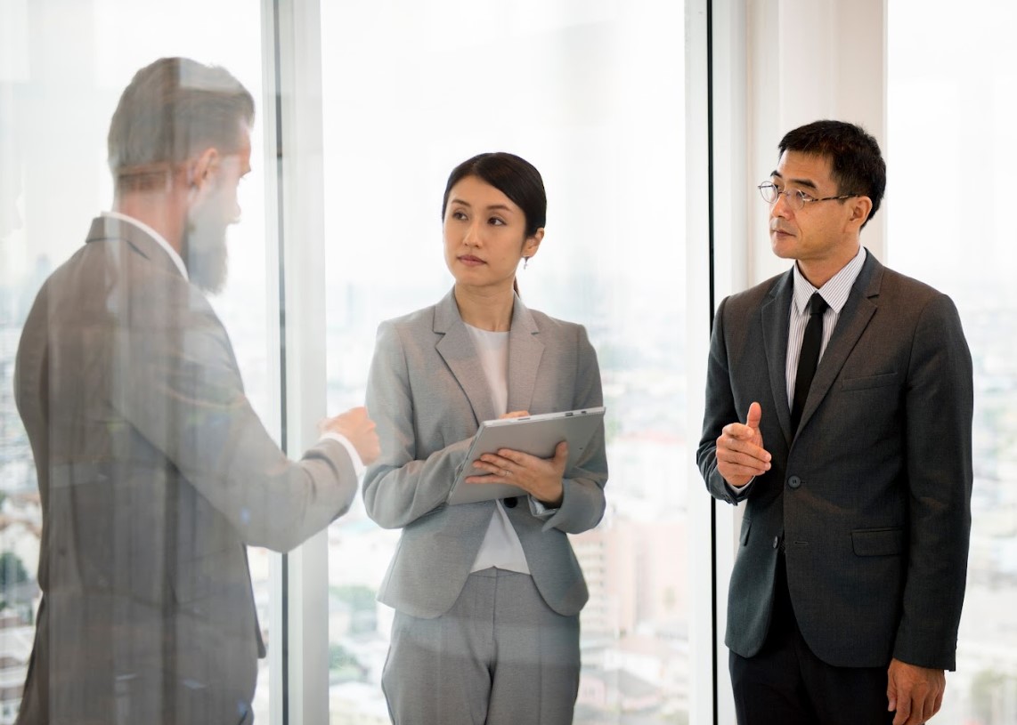 Corporate secretary listening attentively during a business discussion with two male colleagues in a modern office setting.
